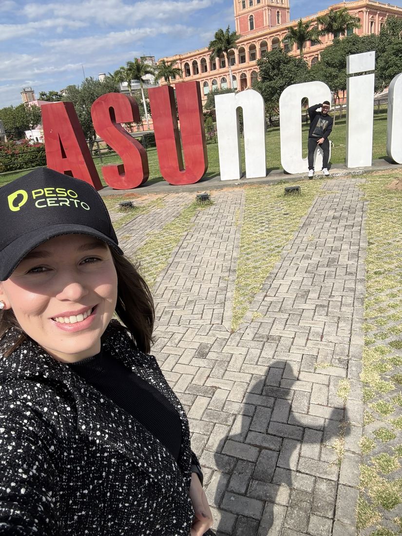 Ela de boné sorrindo em frente ao letreiro de Asunción