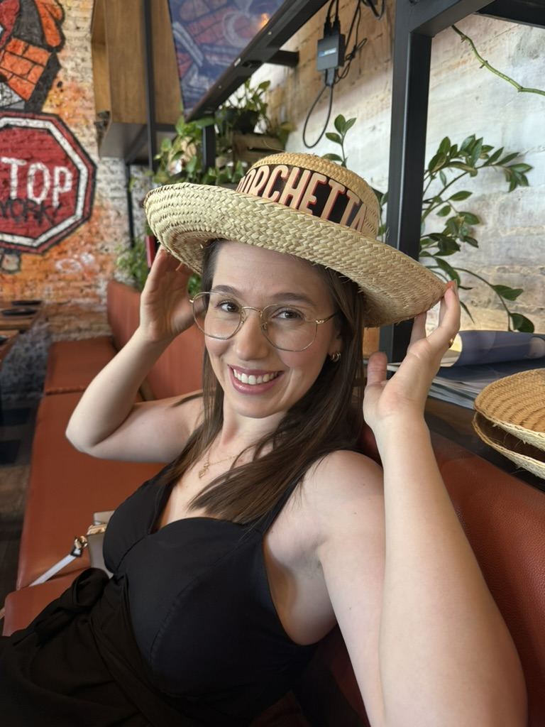 Pâmela sorrindo com um chapéu de palha em um restaurante