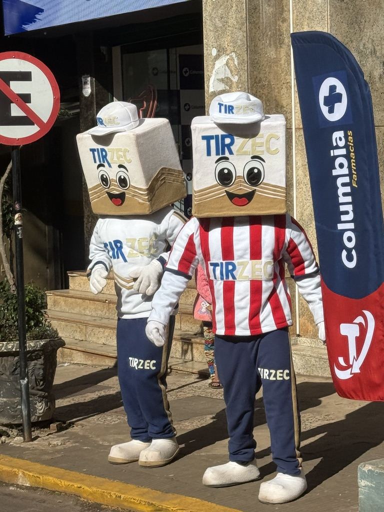 Dois mascotes fantasiados na calçada, um com camisa listrada vermelha e branca