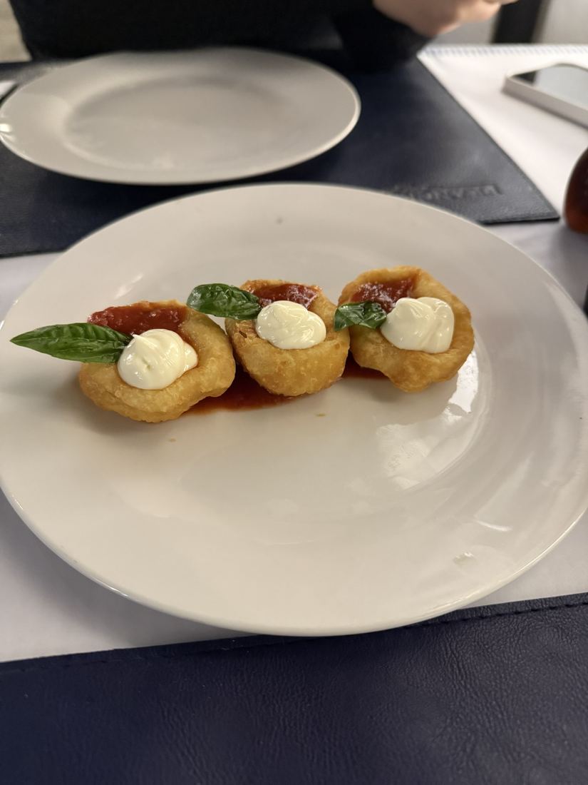 Prato com pequenos petiscos fritos cobertos com creme e manjericão
